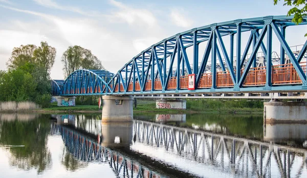 Niebieski most dla pieszych z pomarańczowymi balustrady jest pięknie odzwierciedlony w rzece. — Zdjęcie stockowe