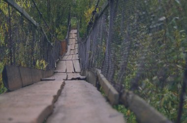 Yağmurdan sonra sonbahar ormannehir üzerinde parlak ahşap asma köprü. Eski tehlikeli asma köprü 