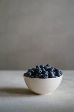 Fildişi kasede koyu gri arka planda taze yaban mersini. Tatlı olgun meyvelerin tazeliği