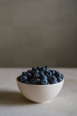 Fildişi kasede koyu gri arka planda taze yaban mersini. Tatlı olgun meyvelerin tazeliği