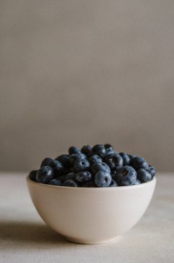 Fildişi kasede koyu gri arka planda taze yaban mersini. Tatlı olgun meyvelerin tazeliği