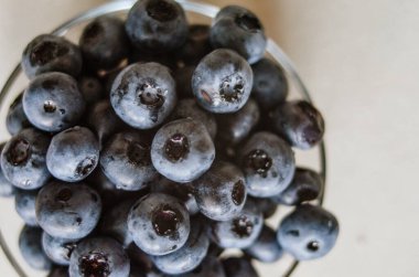 Gri arka planda cam kasede taze yaban mersinli siyah makro. Tatlı olgun meyvelerin tazeliği