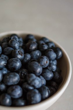 Gri arka planda beyaz kasede taze toplanmış yaban mersini makrosu. Tatlı olgun böğürtlenler yakın 