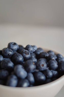 Mavi arka planda beyaz kasede su damlaları olan taze toplanmış yaban mersinli bir makro. Tatlı olgun böğürtlenler beyaz arka planda kapanıyor
