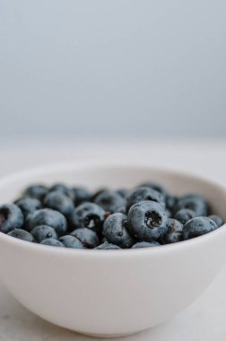 Mavi arka planda beyaz kasede taze toplanmış yaban mersini makrosu. Tatlı olgun böğürtlenler fildişi tabaklara sarılmış. 