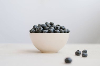 Mavi arka planda beyaz kasede taze toplanmış yaban mersini. Tatlı olgun böğürtlenler yakın 