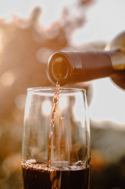 Kırmızı şarabı bardağa dökerek günbatımına ve asma tarlasına karşı