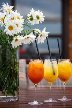 ahşap masa meyve kokteyl ve kenarındaki çiçek dolu vazolar vardır