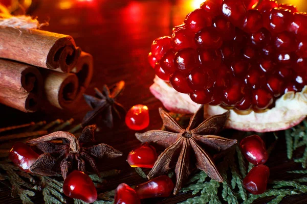 Anise, pomegranate seeds and cinnamon sticks on a wooden table with colorful backlighting. Selective focus. Background for new year greeting card — Stock Photo, Image