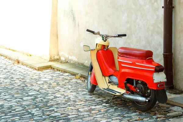 Un ciclomotore rosso si erge vicino al muro sul marciapiede della città vecchia Fotografia Stock