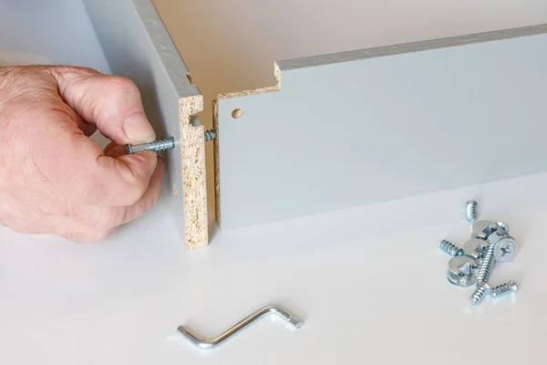 Der Prozess der Estrich zwei Wände der Küche Box bei der Montage von Möbeln. Eine der Schrauben ist bereits angezogen, die zweite wird von männlichen Händen angezogen. Nahaufnahme — Stockfoto