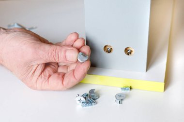 Yaşlı bir adamın elleriyle bir mutfak kutusu montaj süreci. Kutunun ön cephesinin duvarlarla bağlantısı