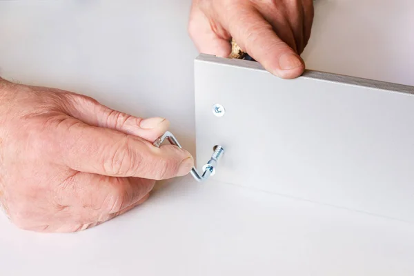 The process of screed two walls of the kitchen box when assembling furniture. One of the screws is already tightened, the second is tightened by male hands. Close-up — Stock Photo, Image