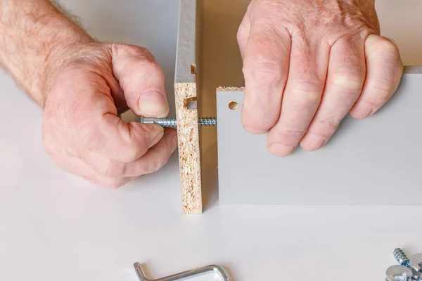 The process of assembling a kitchen box by the hands of an elderly man. Tie hex key box walls — Stock Photo, Image