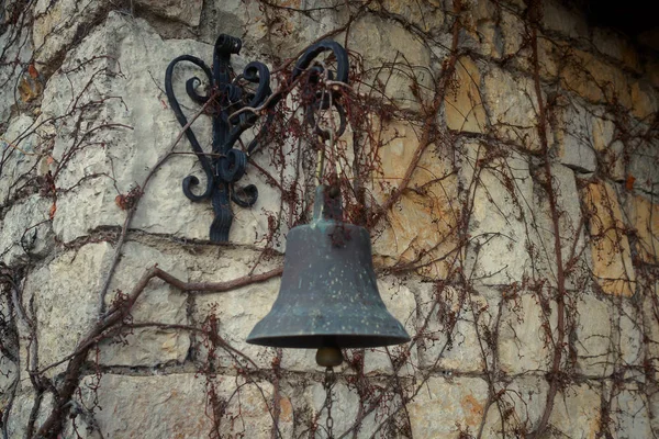 The bell hangs on the old wall in the vine. Tinted
