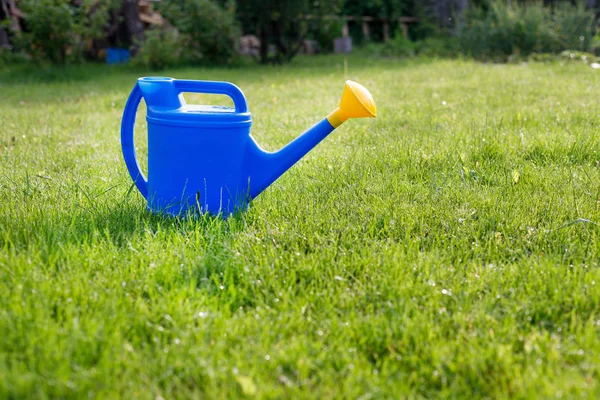 Mavi plastik sulama güneşli bir sabah yeşil bir çim üzerinde sarı bir lens ile olabilir — Stok fotoğraf