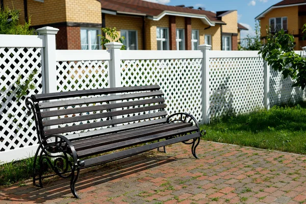 Banc en bois sur le fond d'une clôture en plastique blanc dans un village de campagne — Photo