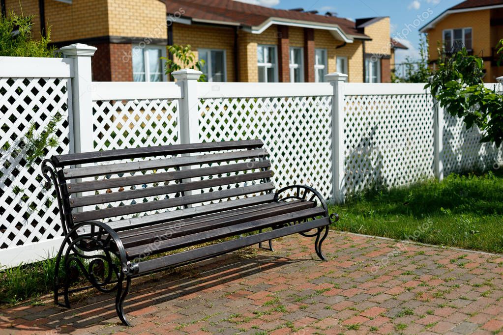 Wooden bench on the background of a white plastic fence in a country village