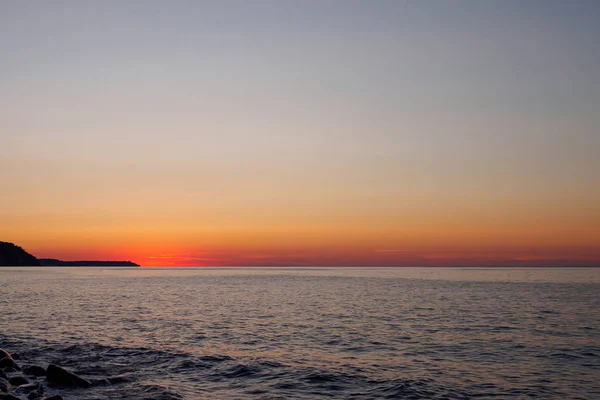 Прекрасний захід сонця і моря. Яскраво-помаранчеве сонце спустилося до лінії горизонту. Останні промені сонця відображаються у темній воді . — стокове фото
