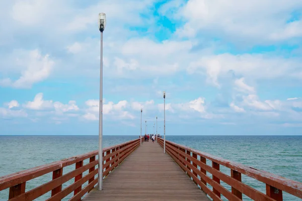 Piercing de mar con un muelle equipado con barandillas de madera y linternas. Cielo azul con nubes de cúmulos blancas . — Foto de Stock