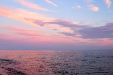 Güzel bulutlu gün batımı ve deniz manzarası. Pembe ve mavi gökyüzü akşam vakti karanlık sularda yankılanır.