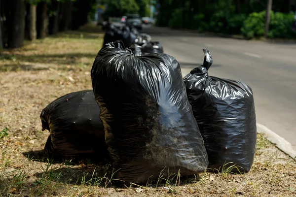 Large black trash bags filled with garbage are on the road. Clean area concept. — Stock Photo, Image