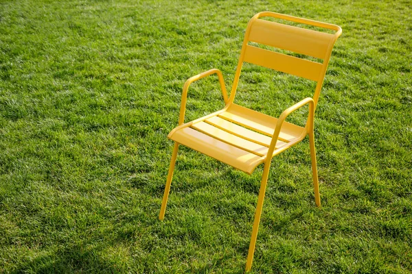 Silla de metal amarillo se encuentra en un césped con hierba verde —  Fotos de Stock