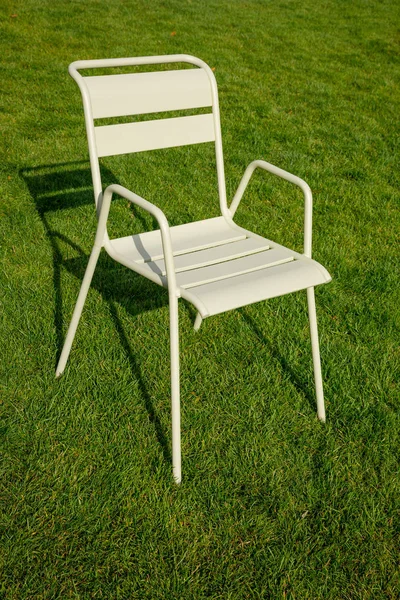Uma cadeira de metal bege fica no gramado. Longas sombras duras na relva verde. Tema urbano. Tema da solidão — Fotografia de Stock