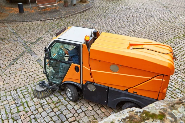 street cleaning machine sweeping a cobblestone road