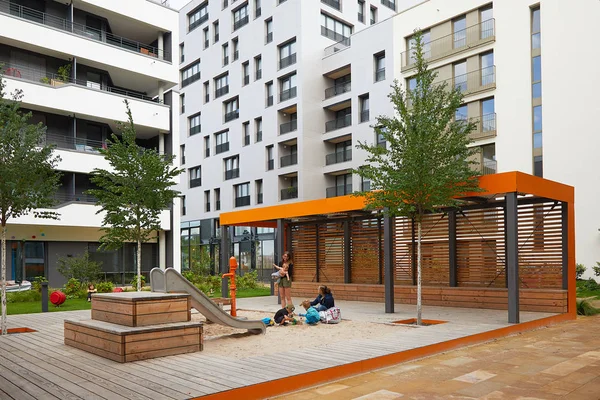 Heilbronn, Alemania - 12 de agosto de 2019. Las mamás con niños pequeños juegan en el arenero en el patio de recreo entre edificios modernos. La imagen de un espacio urbano acogedor . —  Fotos de Stock