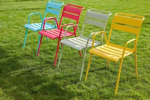 Four multi-colored chairs stand on a green lawn on a summer evening. Image of a comfortable place to relax in an urban environment. Sunset light, long shadows. — Stock Photo, Image