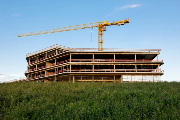 A construction crane and a erected frame of the building against the blue sky. Image of the construction of a residential building, hotel, shopping center, office building, other commercial property.