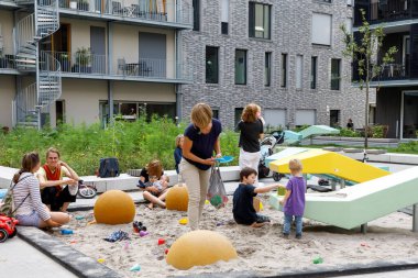 Heilbronn, Almanya - 12 Ağustos 2019. Küçük çocuklu anneler, modern binalar arasındaki oyun alanında ki kum havuzunda oynarlar. Rahat bir kentsel alan görüntüsü