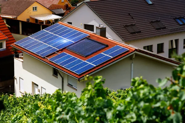 Binanın kiremitli çatısındaki güneş panelleri. Üzüm yaprakları arasından üst manzara. Alternatif enerji tasarımı. Seçici odak.