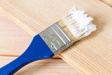 Beyaz boyalı mavi fırça açık ahşap bir tahtanın üzerinde duruyor. Evdeki tamiratın başlangıcı. Seçici odak, boşluğu kopyala