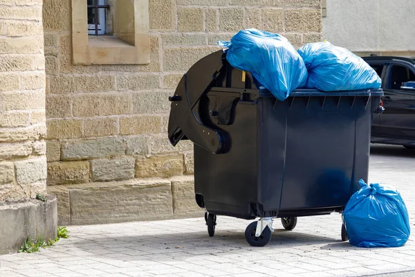Black Plastic Dumpster Full Blue Trash Bags Street Close — Stock Photo, Image