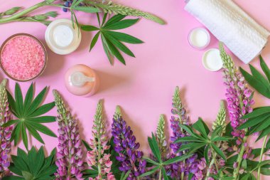 Güzellik kozmetik ürünleri, idrar çiçekleri ve pembe arka planda yeşil yapraklar. Düz yatıyordu. Boşluğu kopyala