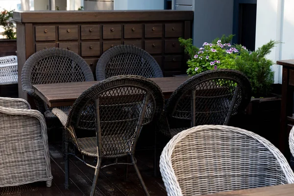 Wicker chairs, a wooden table and a chest of drawers for an outdoor cafe. Empty wooden table and wicker chairs in an outdoor cafe awaiting the visitors after quarantine during the COVID-19 pandemic