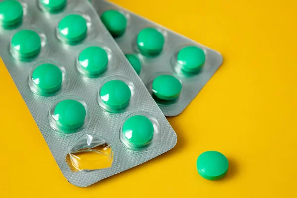 Blisters of green pills and separately one pill on a yellow background. Concept of starting a course of medication and vitamins — Stock Photo, Image