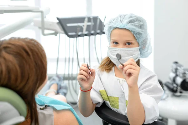 Little girl switched roles with her female dentist. Caucasian child holding dental instruments in her hands