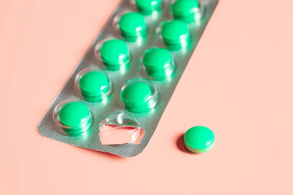 Blister of green pills and separately one pill on a pink background. Concept of starting a course of medication and vitamins. Isolated. Selective focus