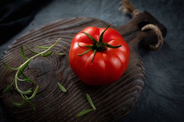 Olgun organik domates ve biberiye filizi eski bir kesim tahtasının üzerinde. Domatesin içinde bir çatlak. Seçici odak.