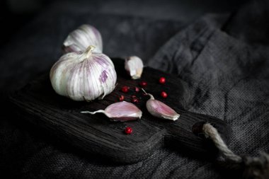 Mutfak temalı bir tasarım için koyu bir arka plan, sarımsak kafa ve doğrama tahtasındaki sarımsak karanfilleridir. Boşluğun kopyası.