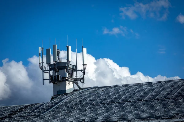 4G, 5G telecommunications transmitters on a roof of a building. Cellular base station with transmitter antennas on a telecommunication tower on against a blue sky with clouds — Stock Photo, Image
