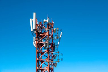 Kırmızı telekomünikasyon kulesi 4G, 5G vericili. Telekomünikasyon kulesinde mavi gökyüzüne karşı verici antenleri olan bir baz istasyonu. Yakın plan.