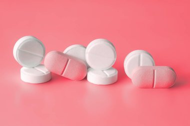 White and pink pills on a red background. Weight loss products, vitamins, hormones or sedatives, Womens health concept. Close-up, selective focus. clipart