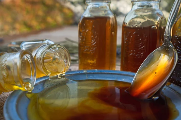 Close up of honey on a plate, and honey in bottles in a garden