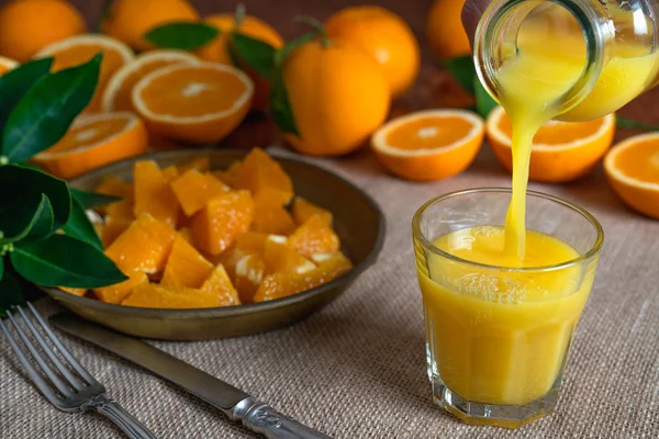 Oranges sliced, orange leaves and glass of orange juice on a kitchen table with  rustic background