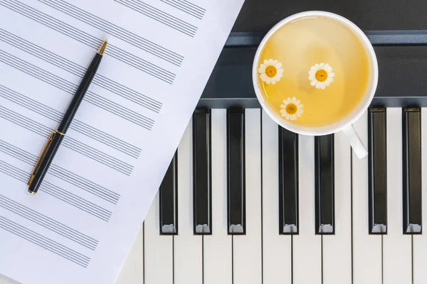 Tasse Kamillentee auf einem Klavier, Notenblatt und Stift. Draufsicht, c — Stockfoto