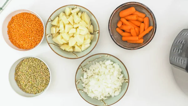 Chopped onion, chopped potatoes, carrot, and lentils close up in bowls, view from above. Lentil soup recipe, ingredients on kitchen table